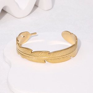 Minimalist 18k gold plated stainless steel feather open cuff bangle on a white pedestal