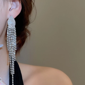 Close-up of sparkling silver jellyfish tassel earrings worn with teardrop diamond stud