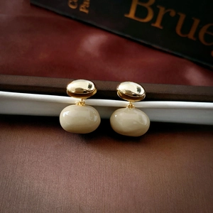 Detail of vintage irregular gold-plated drop oil earrings with cream-colored oval pendants