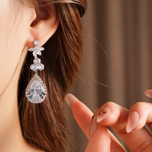 Detail of silver drop earrings with white pear-cut stones worn by a model in soft light