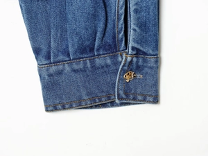 Détail du poignet d'une chemise en jean bleue avec coutures jaunes et bouton doré