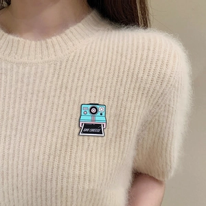 Cartoon polaroid camera enamel pin with Say Cheese text on beige knit sweater