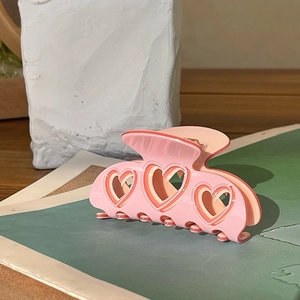 Close-up of a pink Y2K style heart-shaped hollow hair claw clip on a green mat