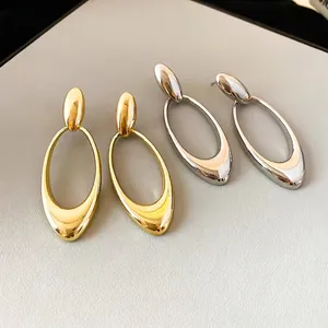 Polished gold and silver oval hollow drop earrings on a premium textured display pad