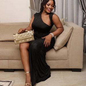 Detail of elegant black slim slit dress with gold snakeskin clutch on a beige sofa