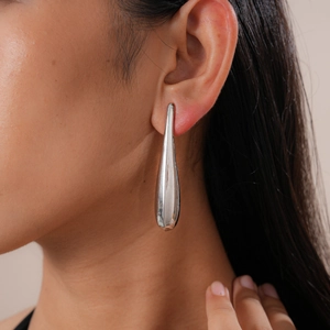 Close-up of polished silver teardrop earring worn by a model in soft natural light