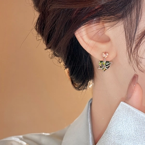 Detail view of heart-shaped green zircon earring with planetary ring on a model