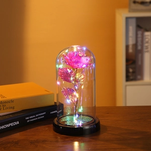 Pink gold-tone rose in a glass dome with LED lights on a black base for home decor