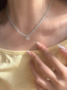 Detail of starfish pendant necklace with light blue beads worn on a model for summer style