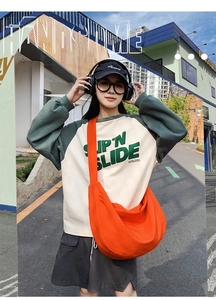 Close-up of bright orange large capacity oxford crossbody bag with sporty streetwear outfit