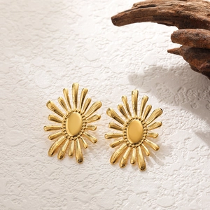 Detailed view of gold sunburst textured earrings on minimalist natural wood background