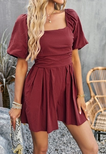 Detail of burgundy square neck romper with puff sleeves and pleated hem in a soft natural light