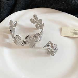 Detailed view of silver flower open cuff bracelet and matching ring set on white porcelain