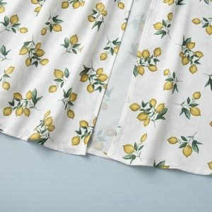Detailed view of summer dress featuring lemon print on white fabric with split hem finish
