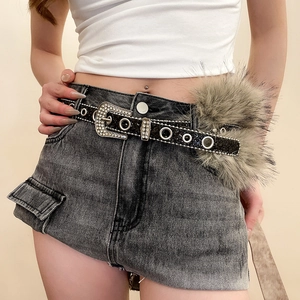 Détail de la boucle de ceinture strass style western et pompon en fourrure sur denim