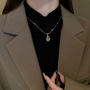 Pendentif goutte en œil de tigre sur chaîne perlée dorée sur un pull à col roulé noir
