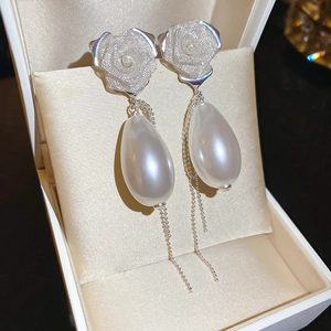 Macro shot of silver rose stud earring with white teardrop pearl and long tassel chains