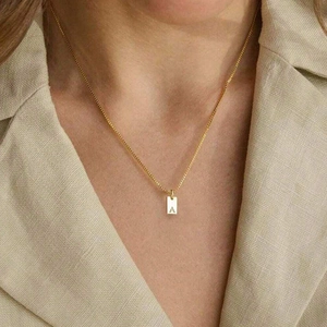 Detail of a gold square pendant necklace with an engraved letter A on a delicate chain