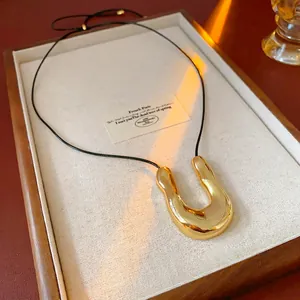 Polished gold U-shaped lava pendant necklace with minimalist black cord on a display tray