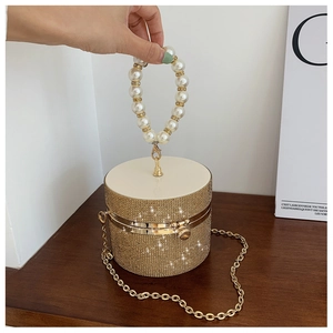 Detail of a champagne gold cylindrical evening bag featuring sparkling rhinestones and pearls