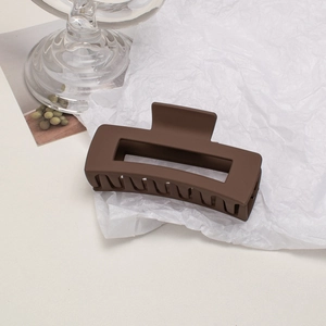 Detailed close-up of a matte brown hollow rectangular hair claw clip on textured background