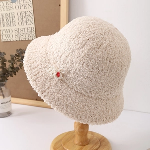 Detalle de gorro de lana de cordero beige con elegante lazo de perlas y corazón.