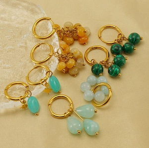 Detail of gold hoop earrings with malachite and teardrop stone pendants on beige fabric