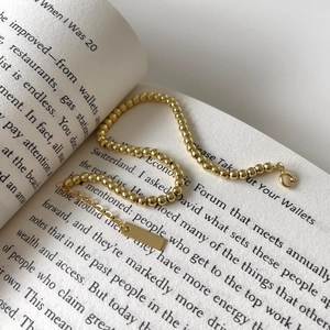 Golden bead bracelet with rectangular charm placed on an open book for an aesthetic look