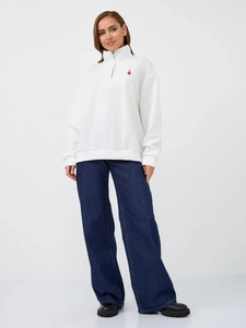 Detail of white quarter-zip sweatshirt with red heart embroidery and high-waist jeans