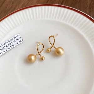 Detail of gold-plated geometric earrings with matte dual spheres on a ceramic plate