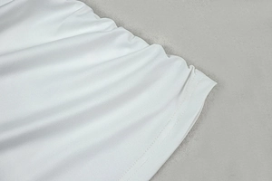 Detail of white knit fabric texture and hemline stitching on asymmetric dress