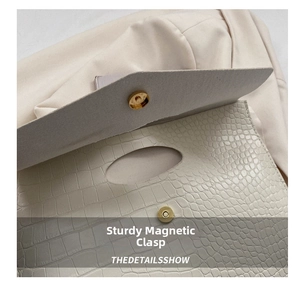 Macro view of golden magnetic closure on cream crocodile embossed leather tote bag