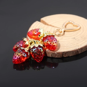 Detailed macro shot of red strawberry charms with gold heart clasp on a wooden base