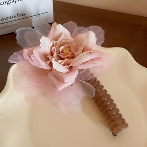 Détail d'une pince à cheveux fleur rose avec spirale ambrée sur un plateau céramique