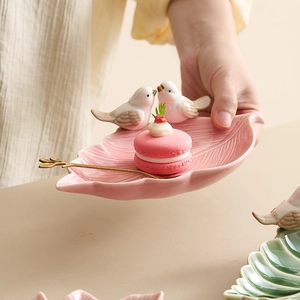 Pink leaf-shaped ceramic jewelry tray featuring two small birds and elegant gold spoon