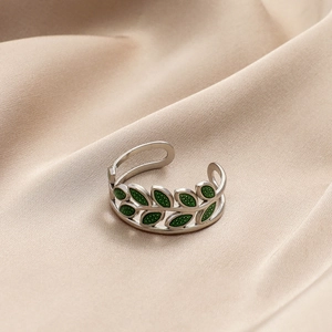 Macro shot of silver leaf ring with green enamel inlay on elegant gold silk fabric