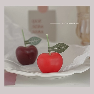 Detalle artístico de velas aromáticas con forma de manzana roja sobre un plato blanco