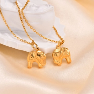 Detail shot of two gold elephant pendant necklaces with intricate carvings on smooth satin
