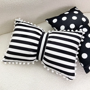 Striped velvet bow pillow with white pom-pom trim on a soft plush background