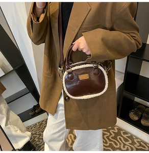 Detail of a brown faux leather pillow bag with white plush trim and metallic nameplate
