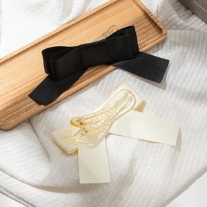 Detail of elegant black and beige ribbon bow hair clips on a wooden tray with soft shadows