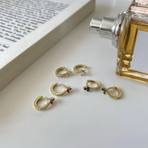 Macro detail of three pairs of gold-plated zircon hoop earrings with colorful gemstones