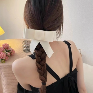 Detail of a creamy white oversized silk bow hair clip styled on a braided hairstyle