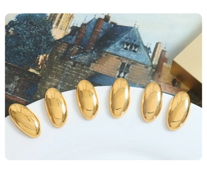 Polished 18K gold plated oval rice-grain stud earrings displayed on ceramic plate