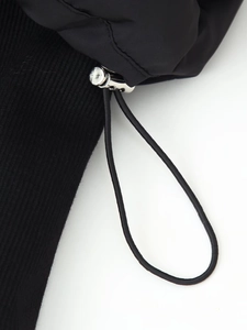 Close-up of black puffer jacket showing ribbed knit cuffs and silver metal drawstring toggle
