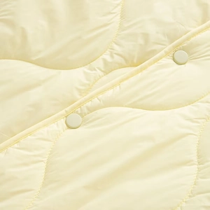 Close-up of pale yellow quilted jacket featuring wavy stitching and matching round button