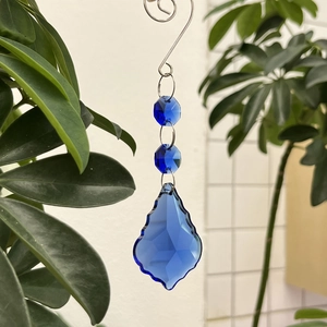 Blue maple leaf crystal suncatcher pendant with faceted teardrop hanging in a garden