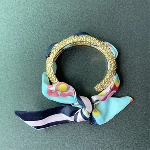 Detail of matte gold open cuff bracelet wrapped with floral sky blue silk scarf