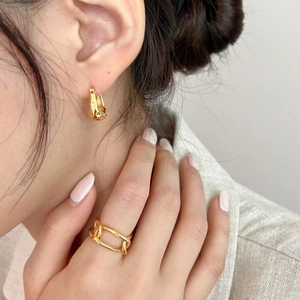 Close-up of a model wearing minimalist golden irregular earrings and a chain ring