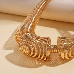 Close-up of golden geometric spring coil necklace with high-shine metallic texture